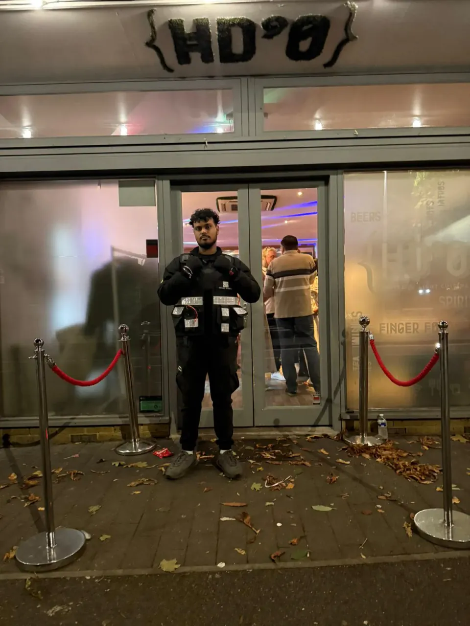 Zentinel SIA door supervisor in tactical vest at a bar entrance at night